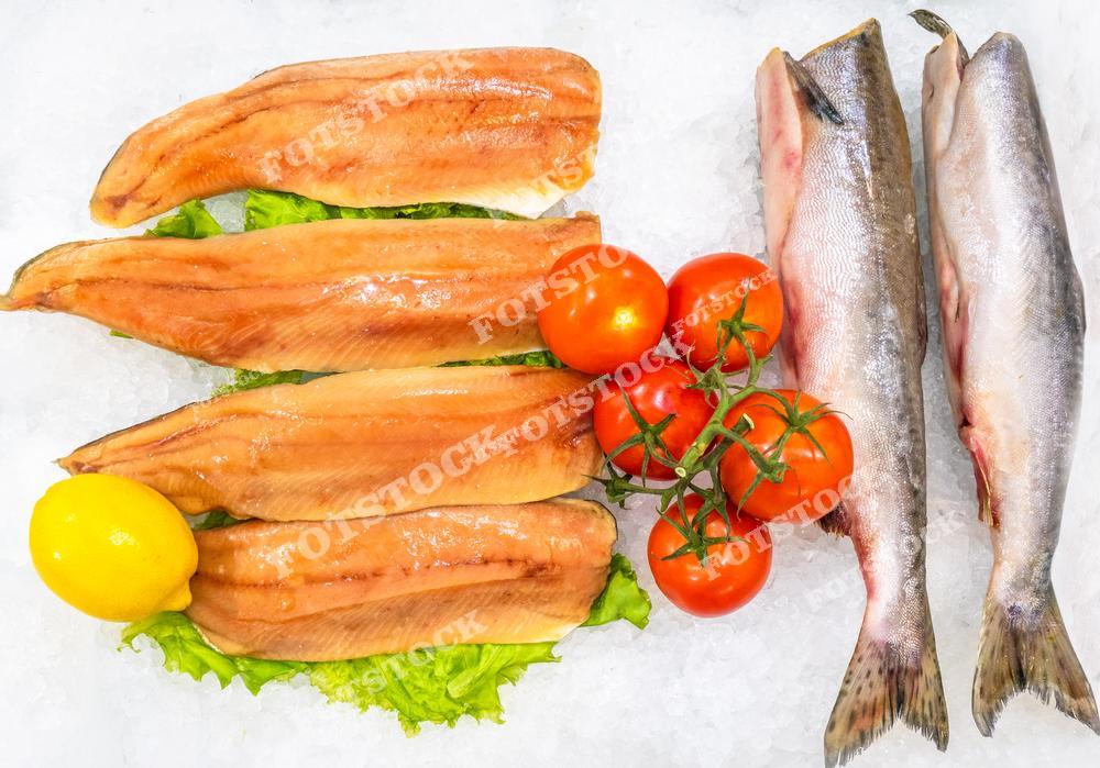 Фотография посвящена морепродуктам. На ней изображена свежая рыба, лежащая на витрине в контейнере с колотым льдом. Морепродукты украшены листьями салата, лимоном и помидорами.